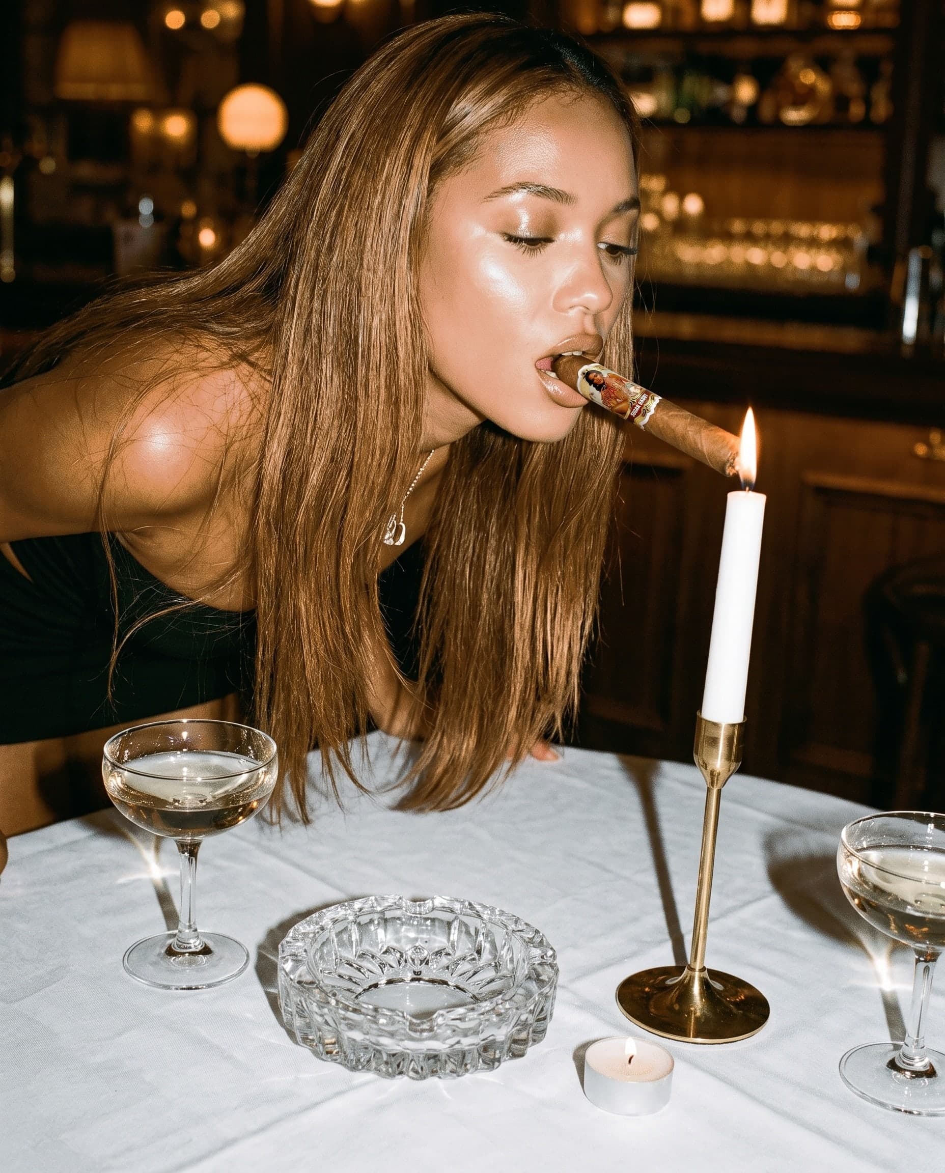 A woman lights a Papasito Sugar Daddy cigar from a candle at a bar table